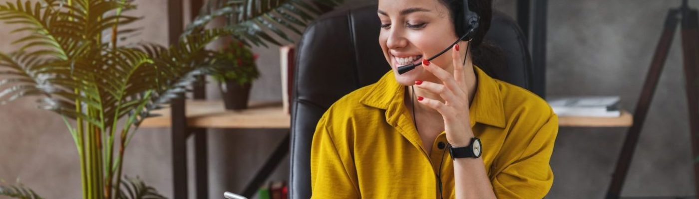 Teleoperator working in home office with laptop and headset on while checking her smartphone